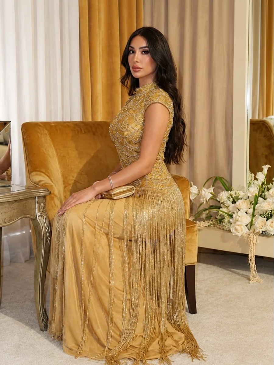 Robe longue dorée brodée de perles assise en salon