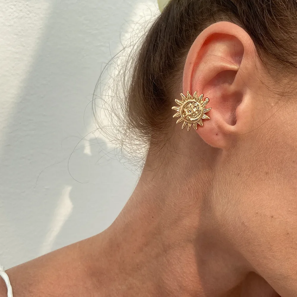 Bijou d'oreille clip doré en forme de soleil porté sans piercing