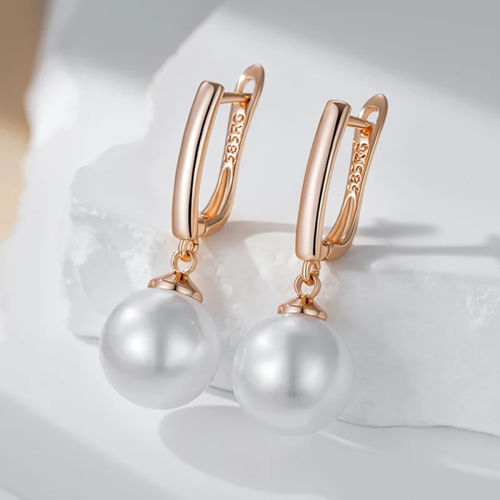 Boucles d'oreilles perle or rose posées sur fond blanc drapé
