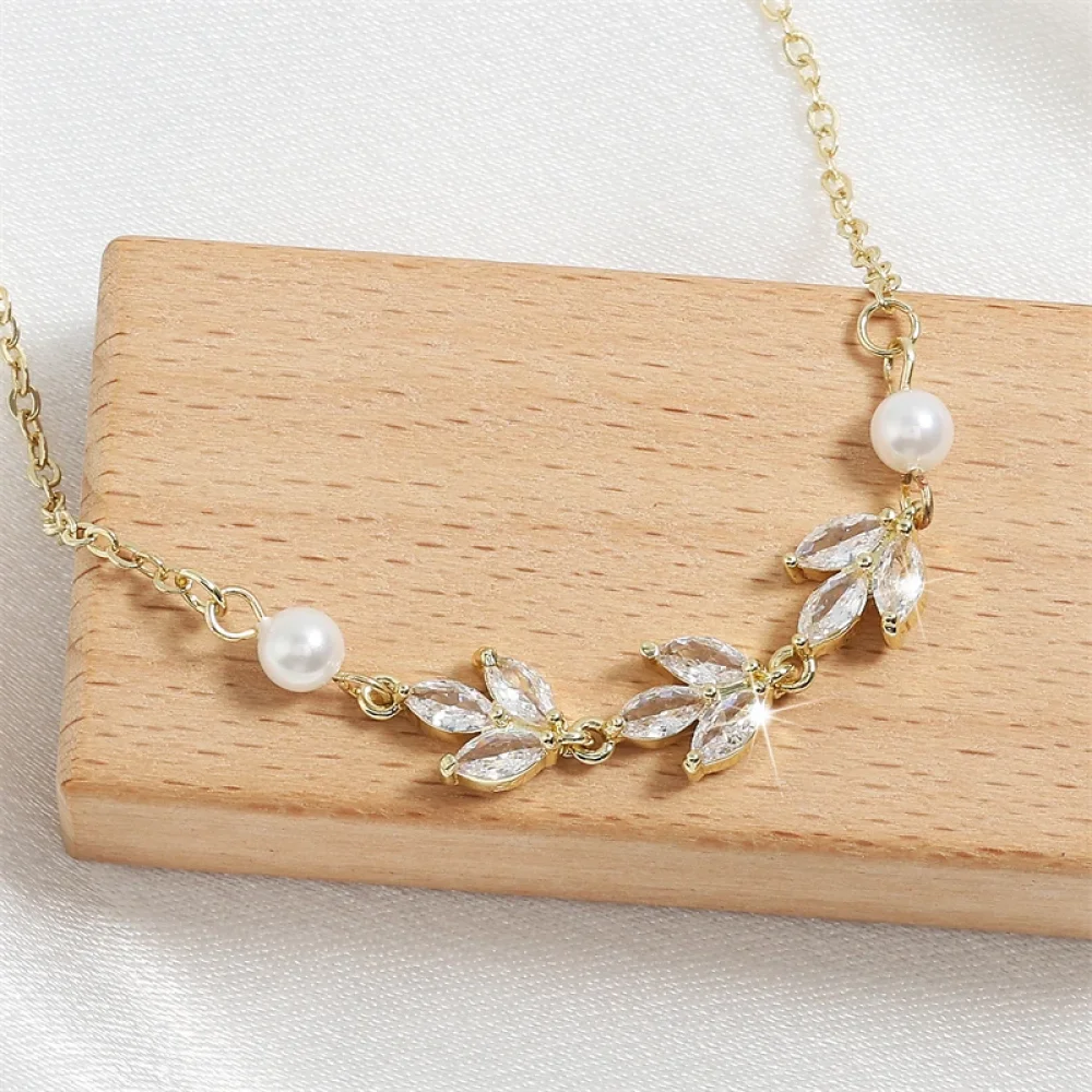 Bracelet doré perles et feuilles zircon posé sur un écrin en bois