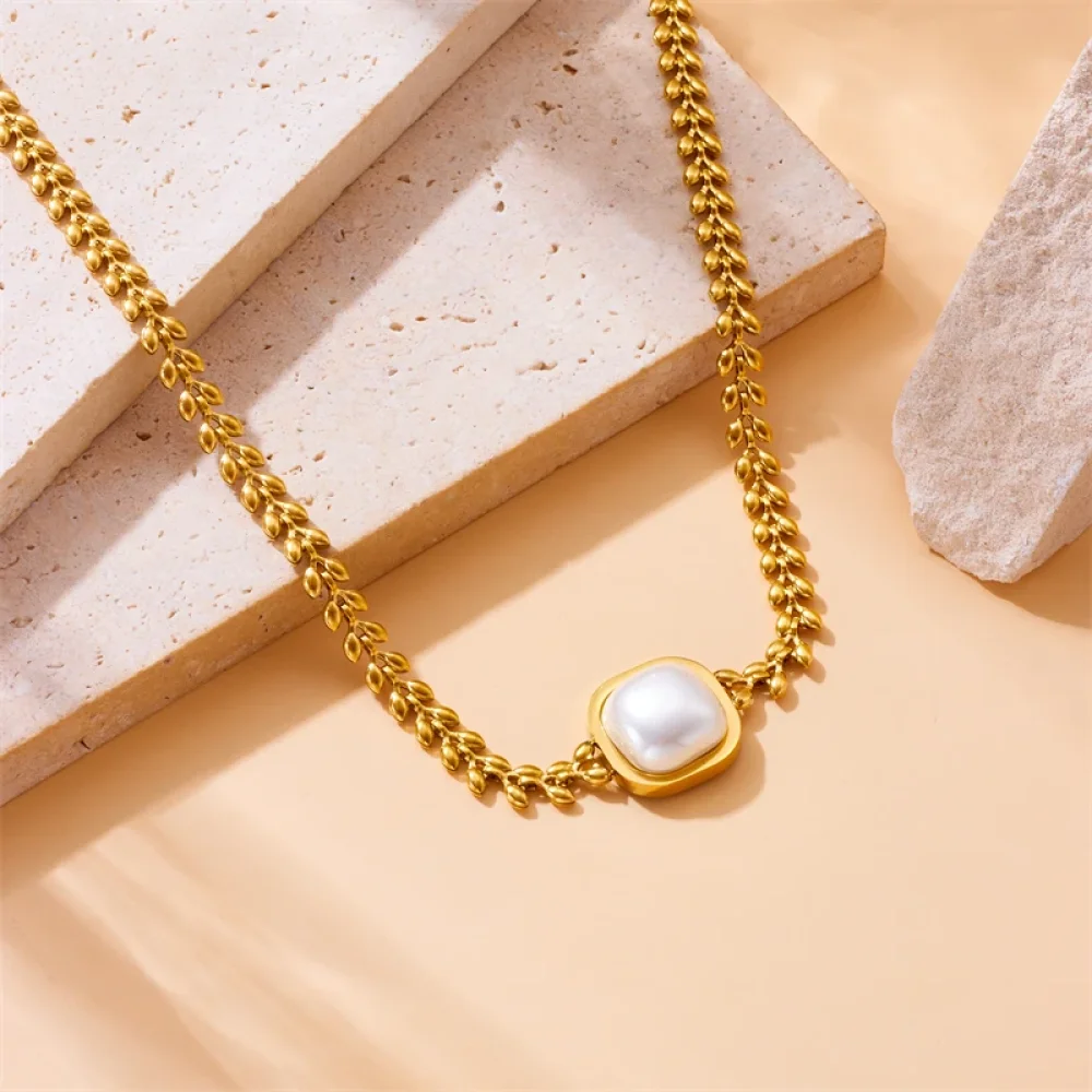 Collier doré grande perle carrée posé sur fond beige