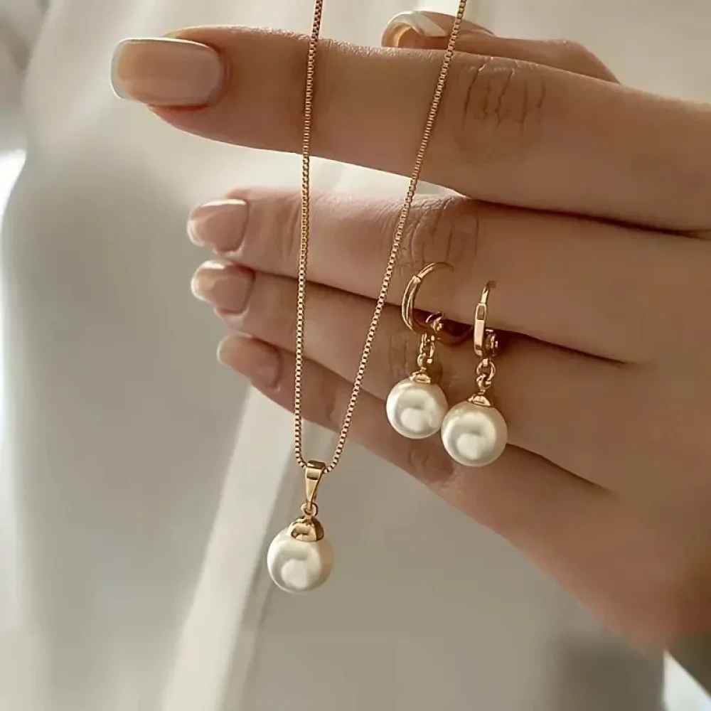 Collier pendentif perle doré et boucles d'oreilles tenus à la main