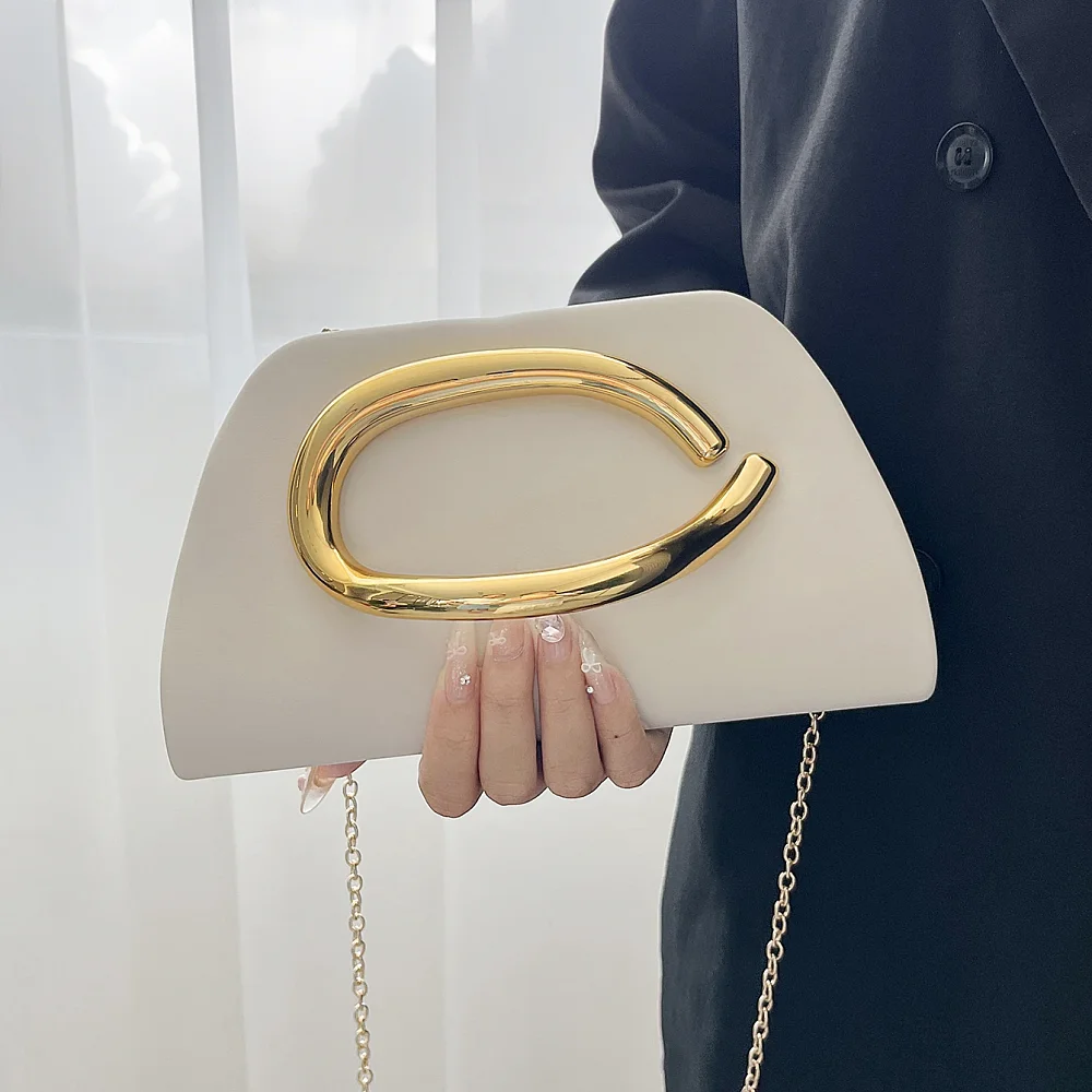 Pochette rigide à anse anneau dorée tenue à la main